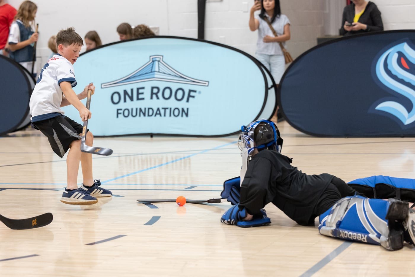 A young Emerald City Ball Hockey player scoring on a diving goalie at Grow the Game Day